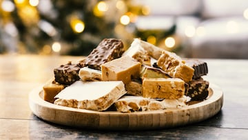 Assorted traditional Christmas nougat on wooden plate with candles in background