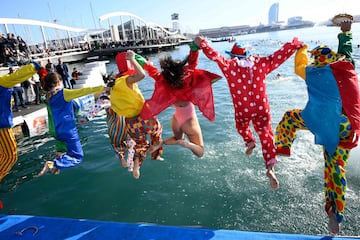 Participantes vestidos de payasos multicolor saltan al agua del Puerto Viejo de Barcelona, lugar donde se disputa la tradicional Copa Nadal.