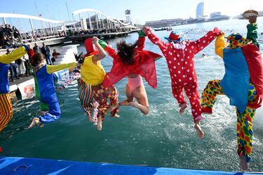 Participantes vestidos de payasos multicolor saltan al agua del Puerto Viejo de Barcelona, lugar donde se disputa la tradicional Copa Nadal.