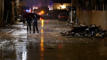 People with umbrellas walk on a mud-covered street, following heavy rains that caused floods, in Paiporta, near Valencia, Spain, November 3, 2024. REUTERS/Eva Manez