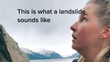 Una excursionista mira con cara de sorpresa a la montaña en Juneau (Alaska, Estados Unidos), con montañas nevadas al fondo y un lago.