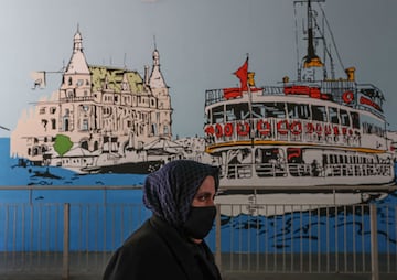 Istanbul (Turkey), 27/04/2020.- A woman wearing a face mask walks past a city-sponsored graffiti mural depicting the historical Haydarpasa Train Station (L) and the famous ferry (R) at a metrobus station in Istanbul, Turkey, 27 April 2020.