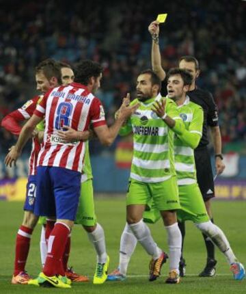 El árbitro Carlos Clos (d) saca tarjeta amarilla al centrocampista del Atlético de Madrid Raul Garcia (i), durante el partido, de Liga en Primera División, que Atlético de Madrid y Getafe disputan esta noche en el estadio Vicente Calderón.