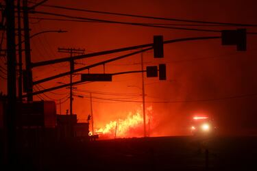 Un camión de bomberos pasa junto a las llamas a lo largo de la Pacific Coast Highway, mientras un incendio forestal arde en el vecindario de Pacific Palisades en el oeste de Los Ángeles.