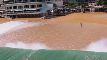 Ola rompiendo en la playa de Acapulco mientras un hombre corre por la playa huyendo