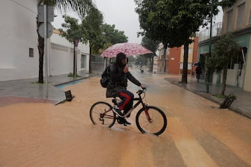 Un ciclista intenta cruzar una calle anegada en el entorno del río Campanillas.