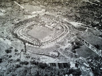 Foto que muestra tres graves problemas del terreno: 1. El formidable cantil de roca que se tuvo que dinamitar en el lado poniente (izquierda) cuya fragmentación fue aprovechada para construir los muros de contención. 2. Las aguas freáticas a solo 10 metros de profundidad en la excavación de la cancha. 3. Los dos accesos originales de 40 y 20 metros, respectivamente, en los extremos de la gran porción que se tuvo que expropiar posteriormente para lograr la gran explanada del lado oriente. 