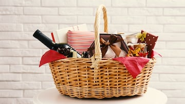 Wicker gift basket with bottle of wine on table near white brick wall