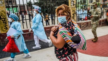 TOPSHOT - A woman carrying her child is seen wearing a face mask while Peruvian health workers pass by the street to test residents at El Agustino district in Lima, on January 7, 2021. - Peruvian Government restarted house-to-house COVID-19 testing in patients over 60 years old this Thursday in vulnerable neighborhoods of Lima and in provincial ones, in search of containing a second wave of the Coronavirus pandemic. (Photo by ERNESTO BENAVIDES / AFP)