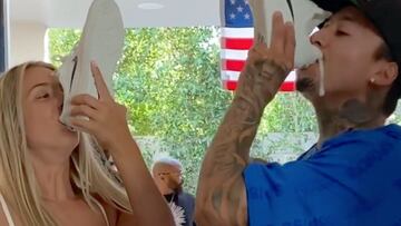Una chica y Nyjah Huston beben cerveza de su zapatilla de Nike Sb blanca en una fiesta, con la bandera de Estados Unidos y varios árboles al fondo.