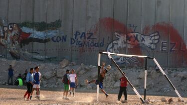 Jóvenes palestinos juegan al fútbol junto a un tramo de la barrera de separación israelí, en la aldea cisjordana de Abu Dis, a las afueras de Jerusalén.