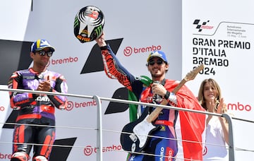 Francesco Bagnaia celebra su triunfo en el podio con una guitarra eléctrica, una bandera de Italia a modo de capa y el casco agarrado con la mano.