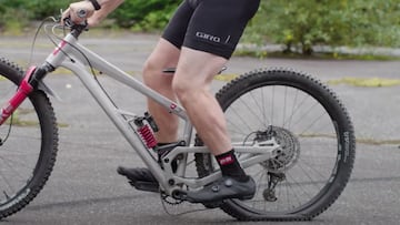 Una bici de MTB Grim Donut forzando suspensi&oacute;n, cadena y neum&aacute;ticos con un ciclista encima, sobre asfalto y con &aacute;rboles al fondo. 