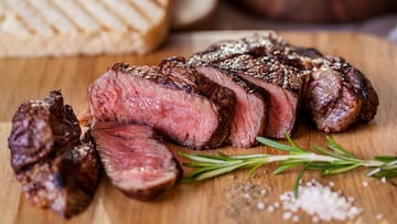 Grilled pork steak pieces with a sprig of rosemary, pepper and salt, fried pieces of bread on a wooden board. Horizontal orientation