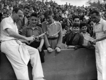 25th May 1950 Jean Borotra (izquierda) y Henri Cochet explican a un grupo de niños cómo coger una raqueta de tenis durante el torneo de Roland Garros en 1950.
