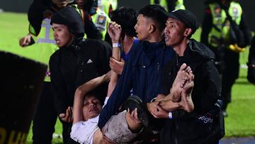 In this picture taken on October 1, 2022, a group of people carry a man at Kanjuruhan stadium in Malang, East Java. - At least 127 people died at a football stadium in Indonesia late on October 1 when fans invaded the pitch and police responded with tear gas, triggering a stampede, officials said. (Photo by AFP)