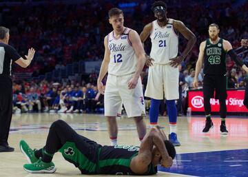 Embiid y T.J. McConnell observando a Marcus Smart que está en el suelo. 