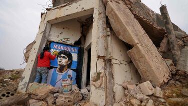 (FILES) In this file photo taken on November 26, 2020 Syrian painter Aziz Asmar draws on the wall of a destroyed home a portrait of famous Argentine footballer Maradona, who passed away yesterday, in the town of Binnish in Syria's northwestern Idlib province. - Diego Maradona's death on November 25, 2020 shook the world of sport. The surprise and pain over the death of the football troubled genius at the age of 60 reinforced his myth and multiplied the tributes that seek to immortalize him. (Photo by Muhammad HAJ KADOUR / AFP)