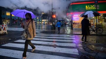 Pedestrians carrying umbrellas cross a street before a pizza restaurant during rain in New York on March 18, 2021. (Photo by Ed JONES / AFP)