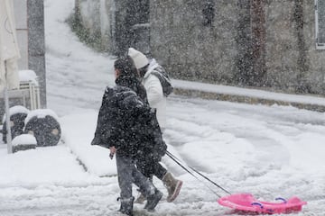 Dos personas caminan con un trineo por la nieve en Castroverde, Lugo, Galicia. La cota de nieve está en 400 metros y ha sido acompañada por un descenso de las temperaturas. La situación más complicada está en las carreteras de la red secundaria de la montaña, donde muchas vías están cortadas al tráfico como consecuencia de árboles que se han desplomado por el peso de la nieve, pero también por las placas de hielo y la nieve en la carretera que dificultan la circulación. Es por eso que la Xunta ha suspendido el transporte escolar y cientos de niños se han quedado sin clase. Además, algunos municipios están sufriendo apagones constantes.