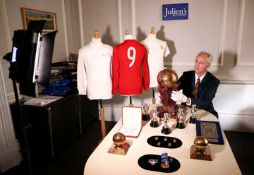 El director ejecutivo de subastas Julians, Martin Nolan, posa junto a varios objetos de la colección Propiedad del patrimonio de Alfredo Di Stéfano antes de ser subastados en Londres. El lote incluye 600 artículos, entre los que destacan camisetas, medallas, monedas, trofeos y placas, entre otros, valorados en casi un millón de euros.