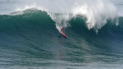El surfista de olas grandes Alberto Ortega, con licra y tabla de surf roja, surfeando una ola grande.