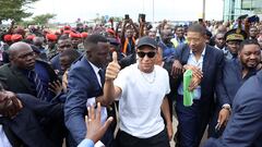 Paris Saint-Germain and France national football team star striker Kylian Mbappe (C) greets crowds gathered outside at the Yaounde Airport in Yaounde on July 6, 2023 as he arrives for a charity visit and a tour of his father's village. (Photo by Daniel BELOUMOU OLOMO / AFP)