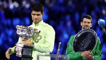 Tennis - Australian Open - Melbourne Park, Melbourne, Australia - February 1, 2026 Spain's Carlos Alcaraz celebrates with the trophy after winning the Australian Open men's singles as Serbia's Novak Djokovic looks on with the runner-up trophy. Alcaraz becomes the youngest man to win all four grand slam titles. REUTERS/Tingshu Wang