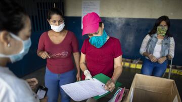 CARACAS, VENEZUELA - APRIL 28: A teacher records on a sheet the data of a mother who has just turned in her daughter's weekly homework at the "Fe y Alegria, Las Mayas" School located in the slum of the Mayas of the parish Coche during the second month of quarantine in the Country on April 28, 2020 in Caracas, Venezuela. Due to the government-ordered coronavirus lockdown, students in Venezuela will have to attend classes remotely until the end of the school year on July 10th. In most cases, teachers connect with their students daily or weekly through e-mail or social media. Online education is a challenge in a country with a very unstable and slow internet service, frequent power outages and low-income households where parents lack of time to spend teaching their kids. (Photo by Leonardo Fernandez Viloria/Getty Images)