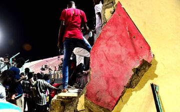 People stand amid a collapsed wall at Demba Diop stadium July 15, 2017 in Dakar as after a football game between local teams Ouakam and Stade de Mbour. adding many more were injured.
