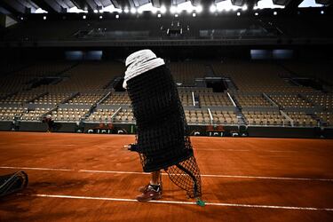 Un miembro del personal de mantenimiento se dispne a colocar una red en la Philippe-Chatrie, la pista principal del complejo Roland Garros, en París. El torneo arrancará el domingo y en los días previos se ultiman todos los detalles. El operario se encuentra detrás de la red, pero por la perspectiva de la foto parece que está enrollada alrededor de su cuerpo.