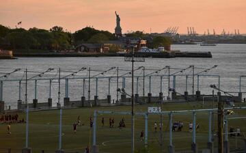 Un partido de ftbol durante la puesta de sol en el Brooklyn Bridge Park en Nueva York con la Estatua de la Libertad al fondo.