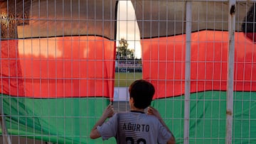 Un niño seguidor del Palestino de Chile mira el campo entre dos banderas palestinas.