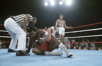 George Foreman intenta levantarse de la lona mientras el árbitro Zack Clayton lo controla durante el combate.