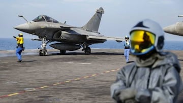 A French navy aircraft handling officer (L), known as a "Chien Jaune" (French for "yellow dog") signals to a Rafale aircraft fighter jet on the flight deck as a firefighter (R) looks on, on the French aircraft carrier Charles de Gaulle, sailing between the Suez canal and the Red Sea on December 19, 2022. - French President Emmanuel Macron will join the French aircraft carrier Charles de Gaulle on December 19, 2022 for the traditional Christmas party with the troops, before attending a regional conference in Jordan on December 20, the Elysee presidential palace announced. (Photo by Ludovic MARIN / POOL / AFP) (Photo by LUDOVIC MARIN/POOL/AFP via Getty Images)