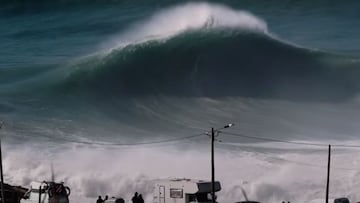 Una ola gigante a punto de romper en Praia do Norte (Nazar&eacute;, Portugal), vista desde el acantilado, con varios coches y autocaravanas, as&iacute; como los palos de luz que hay. 