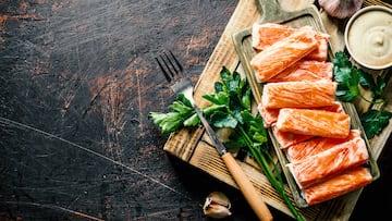 Crab sticks on wooden tray with herbs, garlic and sauce. On dark rustic background