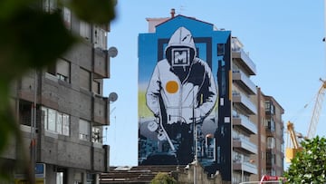 Mural de O Marisquiño pintado en la calle Coruña de Vigo (Galicia, España), de un tipo con sudadera y el logo del festival en la cara, con una tabla de skate bajo el brazo.