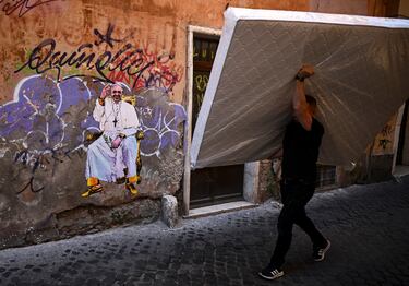 A man carries a mattress near an artwork depicting Pope Francis, following the death of the pontiff, in Rome, Italy, April 22, 2025. REUTERS/Dylan Martinez