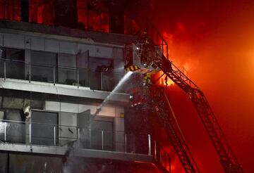 Un incendio de grandes dimensiones arrasa un edificio de 14 plantas generando una gran columna  de fuego y una densa humareda dificultano a los bomberos las labores de extición. En la imagen, una persona atrapada en uno de los balcones del inmueble y un bombero trabajando durante el siniestro.