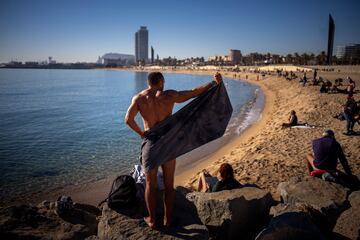 Un hombre se seca con una toalla mientras la gente disfruta del clima clido en la playa, en Barcelona.