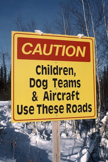 Curiosa señal de precaución en Alaska que advierte a los conductores que la  carretera es transitadas por niños, trineo de perros y aviones. Una combinación peculiar.