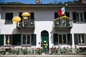 Una espectadora sostiene un paraguas amarillo mientras se encuentra en el balcón de una casa decorada con los colores del Tour de Francia. 