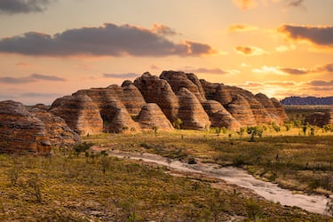 La Cordillera Bungle Bungle, situada en el Parque Nacional Purnululu en el noroeste de Australia, es un asombroso laberinto de cúpulas de arenisca con forma de colmenas gigantes que se elevan hasta 250 metros. Formadas hace unos 350 millones de años, estas estructuras presentan un rayado horizontal único de color naranja y gris oscuro: las franjas naranjas deben su tono a la oxidación del hierro, mientras que las grises están compuestas por capas de cianobacterias que retienen la humedad en la superficie de la roca.