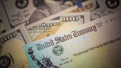Cheque del Departamento del Tesoro de Estados Unidos acompa&ntilde;ado de billetes de cien d&oacute;lares.