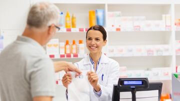 medicine, pharmaceutics, health care and people concept - female apothecary giving senior male customer his purchase in bag at drugstore