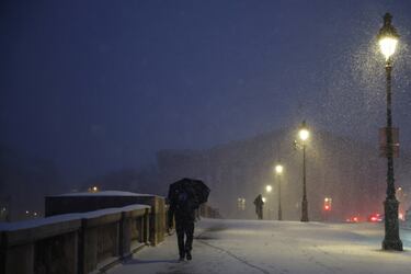 Un hombre se protege de la nieve que cae bajo un paraguas mientras camina por el Puente de la Concordia cubierto de nieve frente a la Asamblea Nacional en París.