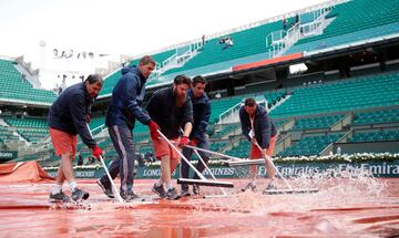 Operarios quitan el agua de la lona sobre la pista de tierra de Roland Garros.