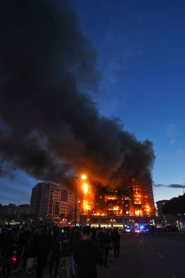 Un incendio de grandes dimensiones arrasa un edificio de 14 plantas generando una gran columna  de fuego y una densa humareda dificultano a los bomberos las labores de extición. Vecinos de la zona observan el inmueble en llamas.