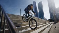 Un ciclista con casco y rastas baja por unas escaleras con la e-bike Serial 1 Mosh/CTY, el modelo m&aacute;s bajo de la gama de bicicletas el&eacute;ctricas de Harley-Davidson. Con unos rascacielos al fondo. 